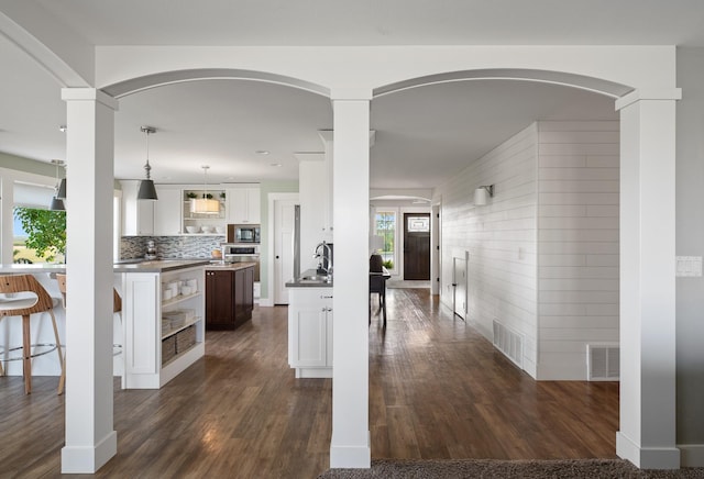 1221 Majestic View Ln, Kalispell, MT 59901 - kitchen featuring stainless steel microwave, open shelves, dark wood-style floors, arched walkways, and wooden walls