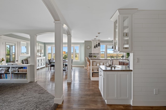 1221 Majestic View Ln, Kalispell, MT 59901 - kitchen featuring ornate columns, arched walkways, a sink, dark wood-style flooring, and glass insert cabinets