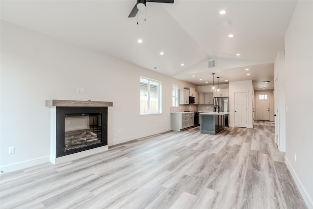 1050 Mill Creek Dr, Bigfork, MT 59911 - unfurnished living room with a ceiling fan, lofted ceiling, light wood-style floors, a glass covered fireplace, and recessed lighting