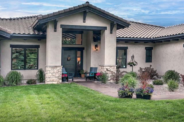 344 Chapman Ln, Bigfork, MT 59911 - doorway to property featuring a lawn, a tiled roof, stucco siding, and stone siding