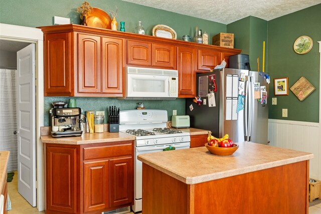 1147 W Woolman St, Butte, MT 59701 - kitchen featuring white appliances, light countertops, a textured ceiling, a center island, and wainscoting