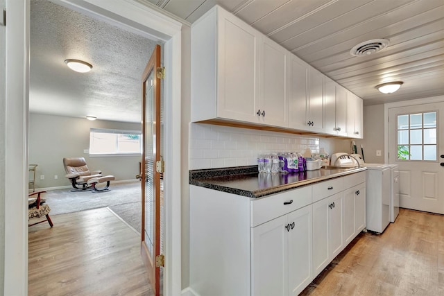 510 Mission St, Stevensville, MT 59870 - kitchen with washer and dryer, light wood finished floors, white cabinetry, decorative backsplash, and dark countertops