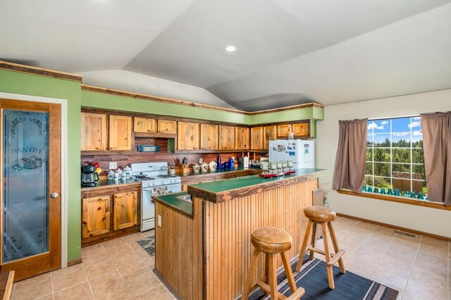 16 Grassland Way, Roundup, MT 59072 - kitchen with white appliances, lofted ceiling, light tile patterned floors, decorative backsplash, and a kitchen bar