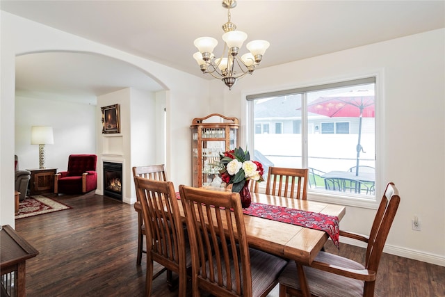173 Empire Loop, Kalispell, MT 59901 - dining area with arched walkways, a chandelier, a lit fireplace, dark wood-style flooring, and baseboards