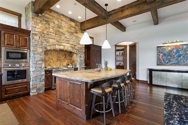 237 Harbor Dr, Bigfork, MT 59911 - kitchen with appliances with stainless steel finishes, beam ceiling, dark wood-style flooring, a center island, and a breakfast bar