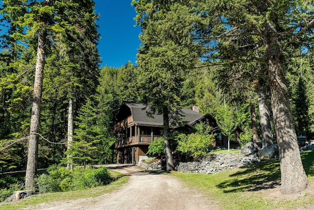 151 Handkerchief Creek Dr, Kalispell, MT 59901 - view of property hidden behind natural elements with driveway, a chimney, a forest view, and a shingled roof