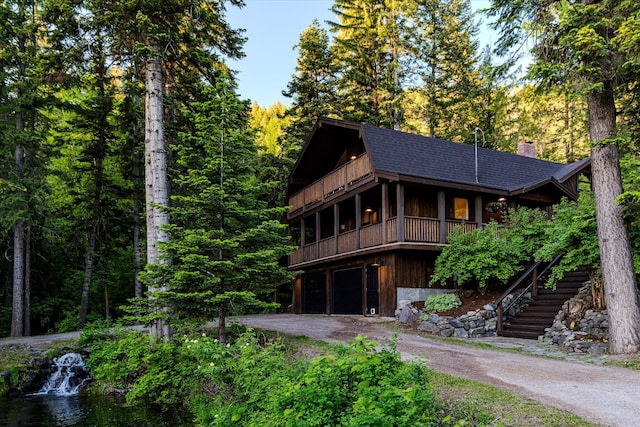 151 Handkerchief Creek Dr, Kalispell, MT 59901 - view of front facade featuring a garage, roof with shingles, asphalt driveway, stairway, and a wooded view