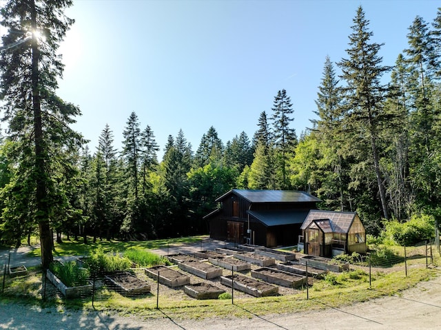 151 Handkerchief Creek Dr, Kalispell, MT 59901 - view of front of property featuring a vegetable garden, an outdoor structure, a greenhouse, and a view of trees