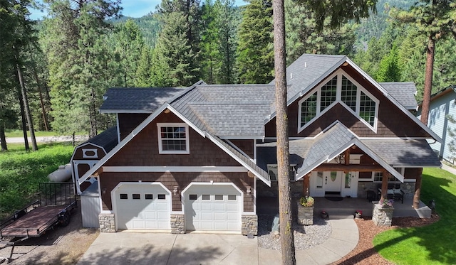 2413 Capstone Ct, Thompson Falls, MT 59873 - view of front of property with covered porch, stone siding, a shingled roof, concrete driveway, and a forest view
