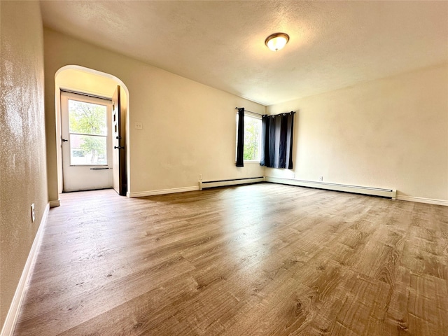 2513 8th Ave N, Great Falls, MT 59401 - empty room with arched walkways, wood finished floors, a baseboard heating unit, baseboards, and a textured ceiling