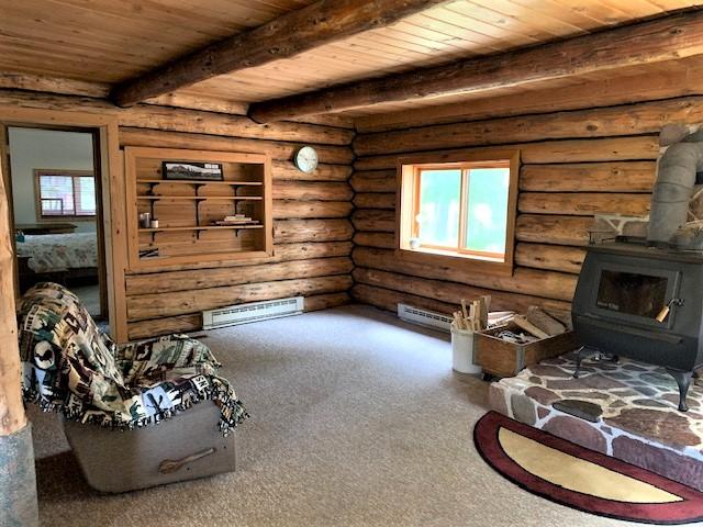 7191 Boy Scout Rd, Seeley Lake, MT 59868 - carpeted living room featuring a wood stove, plenty of natural light, wooden ceiling with exposed beams, and log walls