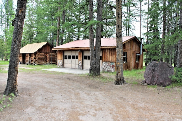 7191 Boy Scout Rd, Seeley Lake, MT 59868 - view of front facade featuring an outdoor structure, a garage, metal roof, stone siding, and board and batten siding