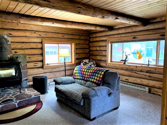 7191 Boy Scout Rd, Seeley Lake, MT 59868 - living area featuring a wood stove, baseboard heating, a wooden ceiling with exposed beams, and log walls