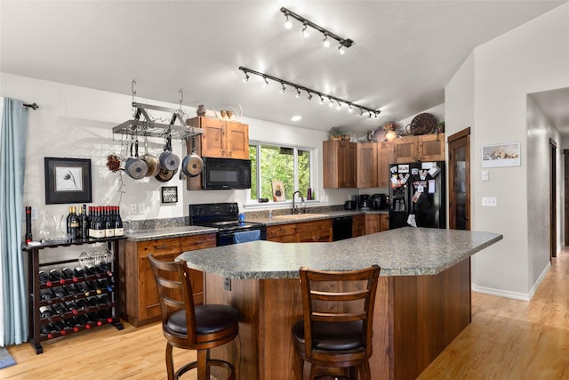 1473 Foothill Rd, Kalispell, MT 59901 - kitchen with black appliances, track lighting, light wood-style floors, dark countertops, and a kitchen bar
