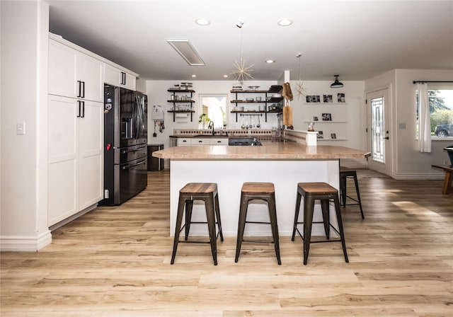 3495 Juniper Dr, Helena, MT 59602 - kitchen with black refrigerator with ice dispenser, a breakfast bar area, white cabinets, light wood finished floors, and a sink