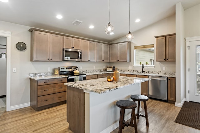 15276 Tyson Way, Frenchtown, MT 59834 - kitchen with appliances with stainless steel finishes, vaulted ceiling, a kitchen bar, light wood-style flooring, and light stone countertops