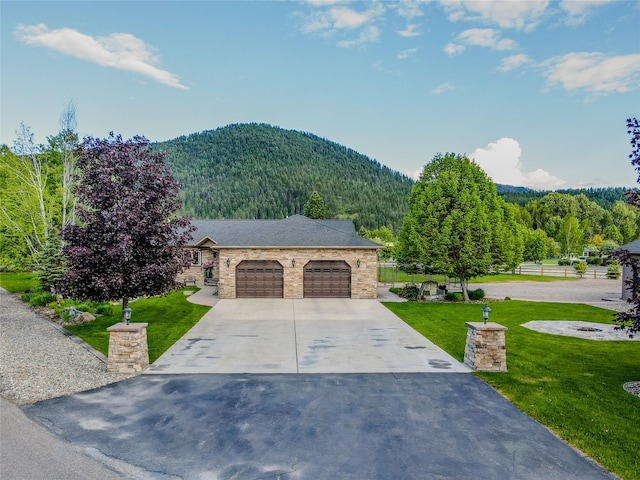 700 Airfield Rd, Libby, MT 59923 - view of front of home with a mountain view, concrete driveway, a garage, stone siding, and a view of trees