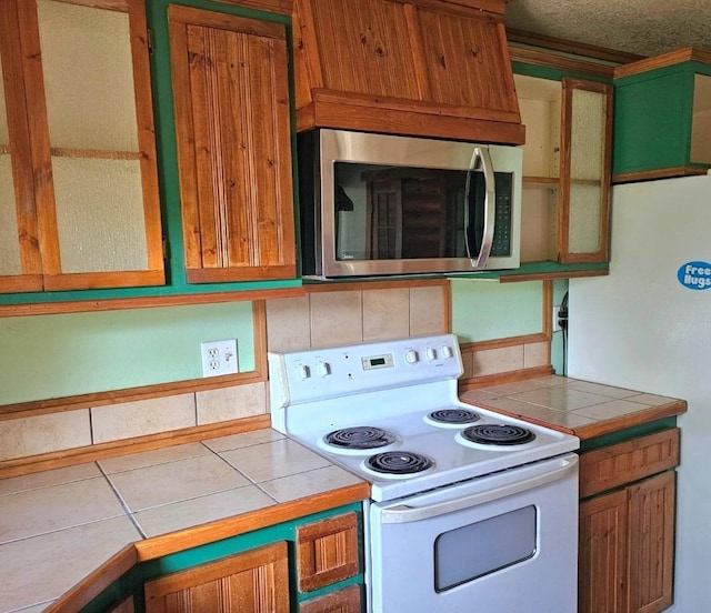 438 Little Mill Creek Rd, Saint Regis, MT 59866 - kitchen with white electric range, stainless steel microwave, tile countertops, and brown cabinetry