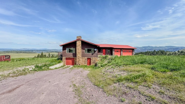 6180 Elkhorn Rd, Helena, MT 59602 - view of property exterior with stone siding, a chimney, dirt driveway, a mountain view, and a garage