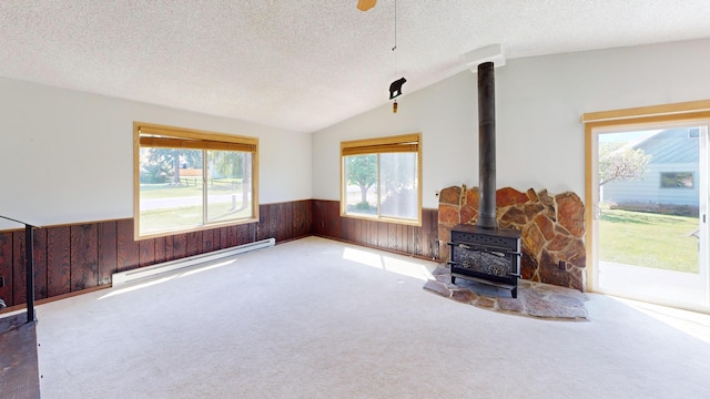 906 11th St E, Polson, MT 59860 - carpeted living area featuring a baseboard heating unit, wainscoting, wood walls, a wood stove, and vaulted ceiling