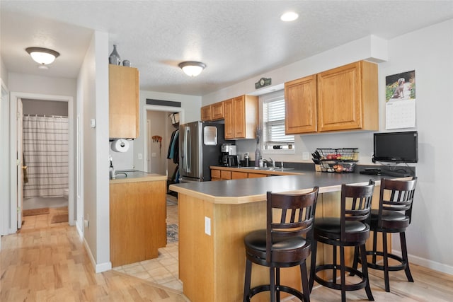 409 Bentley Park Loop, Missoula, MT 59801 - kitchen featuring a kitchen breakfast bar, a peninsula, stainless steel fridge with ice dispenser, light wood-type flooring, and a textured ceiling