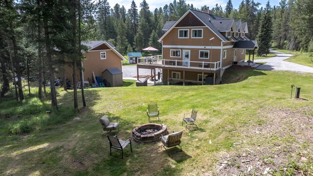 115 Wagon Wheel Rd, Whitefish, MT 59937 - back of property featuring an outdoor fire pit, a wooden deck, a lawn, a storage shed, and a wooded view