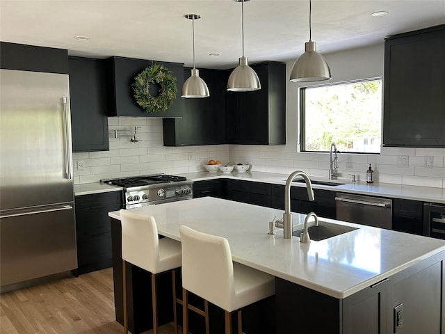 9200 River Rd, Bozeman, MT 59718 - kitchen with stainless steel appliances, tasteful backsplash, dark cabinetry, light wood-style floors, and a center island with sink