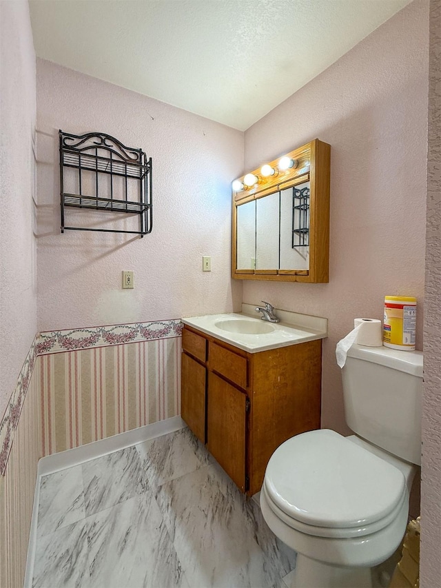802 2nd St SW, Choteau, MT 59422 - half bathroom featuring vanity, toilet, wallpapered walls, and marble look tiles