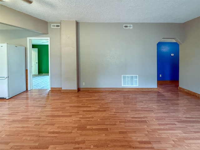802 2nd St SW, Choteau, MT 59422 - unfurnished room featuring arched walkways, light wood-style flooring, a textured ceiling, and baseboards