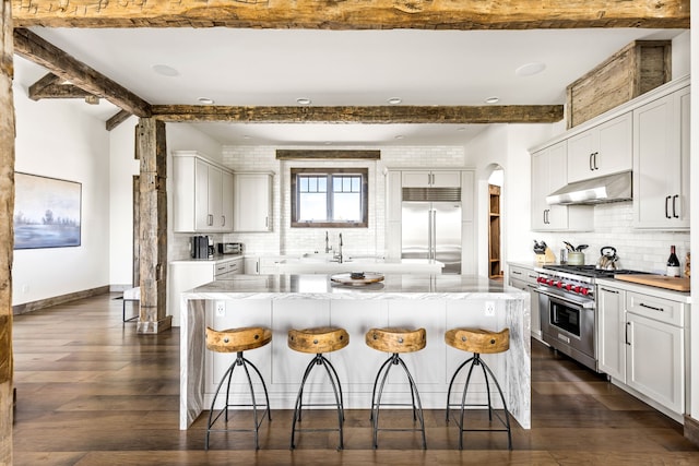 99 Little Belt Way, Belt, MT 59412 - kitchen featuring high end appliances, under cabinet range hood, backsplash, beamed ceiling, and a breakfast bar