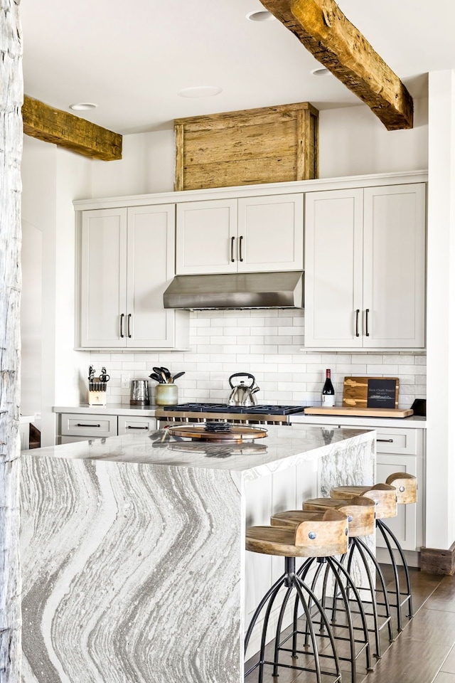 99 Little Belt Way, Belt, MT 59412 - kitchen featuring beamed ceiling, under cabinet range hood, backsplash, light stone countertops, and a kitchen bar