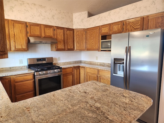 127 Patricia Way, Hamilton, MT 59840 - kitchen featuring appliances with stainless steel finishes, under cabinet range hood, wallpapered walls, brown cabinets, and decorative backsplash