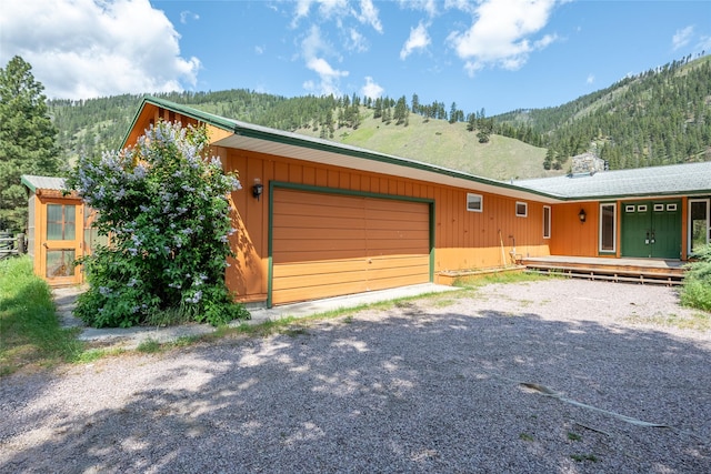 1165 Rock Creek Rd, Clinton, MT 59825 - view of front of house featuring a garage, a mountain view, gravel driveway, and a view of trees
