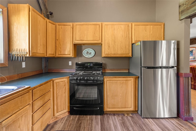 29 Gold Coin Rd, Hall, MT 59837 - kitchen featuring freestanding refrigerator, black gas range, light wood-style flooring, dark countertops, and light brown cabinetry