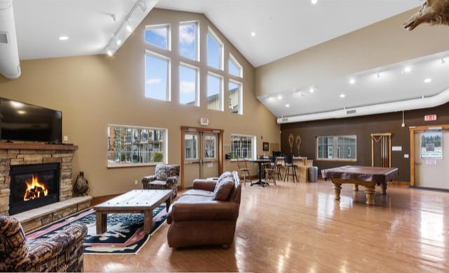 147 Hawthorne Ct Unit B, Whitefish, MT 59937 - living area with pool table, wood finished floors, a stone fireplace, high vaulted ceiling, and track lighting