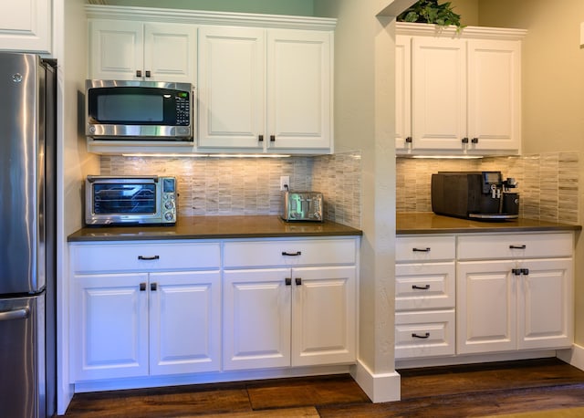 135 E Swift Creek Way, Kalispell, MT 59901 - kitchen featuring appliances with stainless steel finishes, dark countertops, white cabinetry, dark wood-style flooring, and backsplash