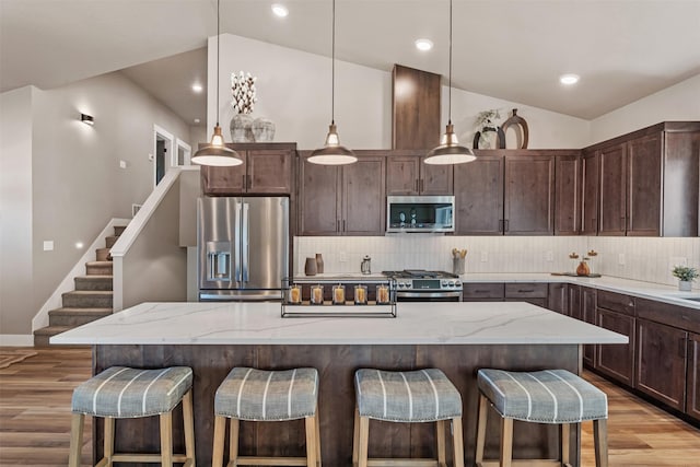 4337 Christian Dr, Missoula, MT 59803 - kitchen featuring stainless steel appliances, light wood finished floors, decorative backsplash, dark brown cabinetry, and a kitchen bar