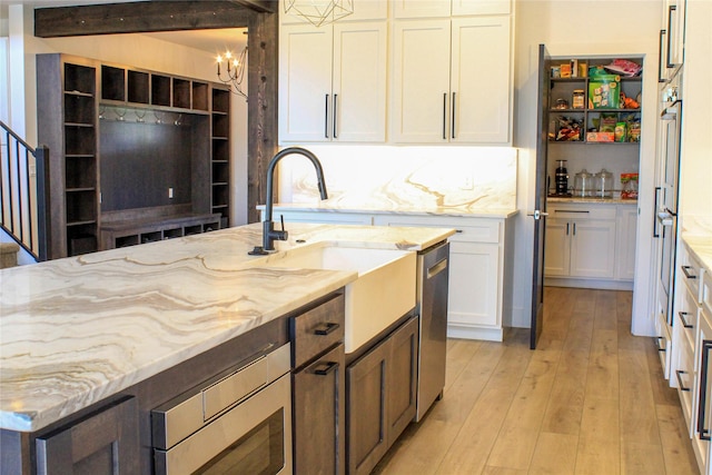 224 Columbia Meadows Dr, Columbia Falls, MT 59912 - kitchen with light stone counters, light wood-type flooring, white cabinetry, a sink, and stainless steel appliances