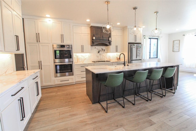 224 Columbia Meadows Dr, Columbia Falls, MT 59912 - kitchen featuring appliances with stainless steel finishes, decorative backsplash, a sink, a kitchen breakfast bar, and light wood-style flooring