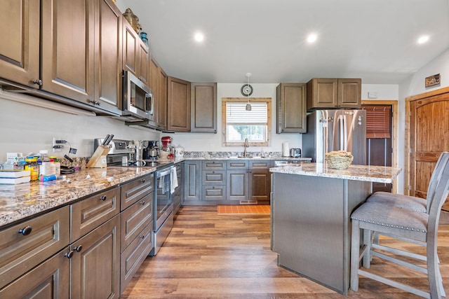 4357 Trumble Creek Rd, Columbia Falls, MT 59912 - kitchen with stainless steel appliances, a kitchen bar, light wood-style floors, light stone countertops, and a kitchen island