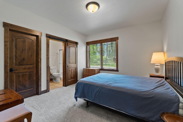 74 Wood Ridge Dr, Columbia Falls, MT 59912 - bedroom with a barn door, light colored carpet, and connected bathroom