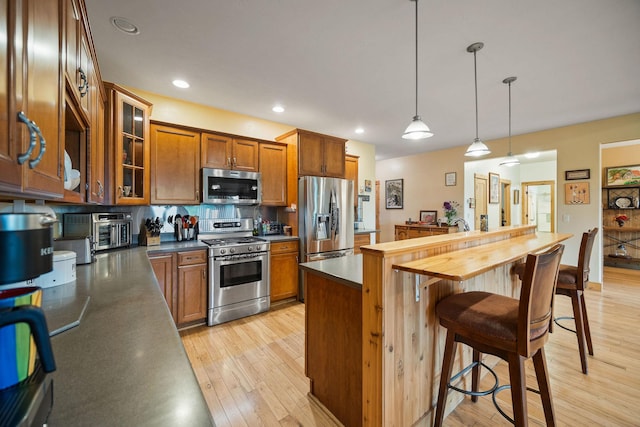 1399 Mackinaw Loop, Somers, MT 59932 - kitchen with stainless steel appliances, brown cabinets, a kitchen breakfast bar, light wood finished floors, and glass insert cabinets