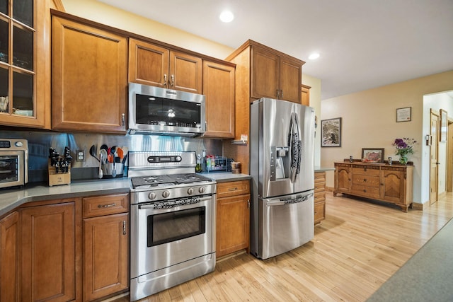 1399 Mackinaw Loop, Somers, MT 59932 - kitchen featuring stainless steel appliances, brown cabinetry, light wood-type flooring, backsplash, and glass insert cabinets