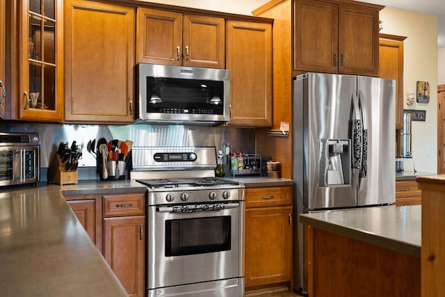 1399 Mackinaw Loop, Somers, MT 59932 - kitchen with appliances with stainless steel finishes, brown cabinetry, backsplash, and glass insert cabinets