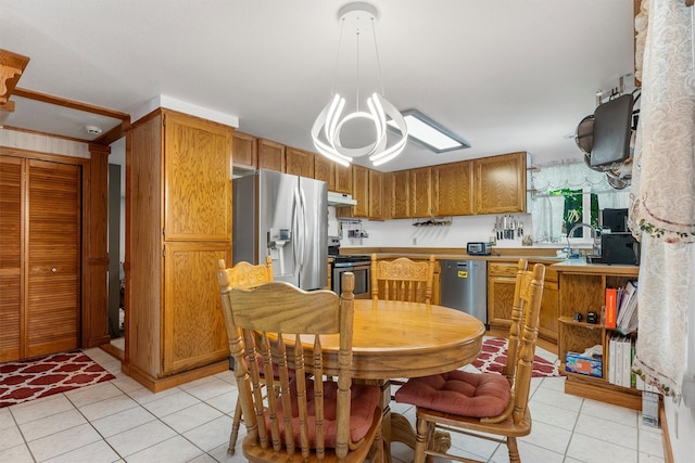 238 Red Fox Rd, Lolo, MT 59847 - kitchen with appliances with stainless steel finishes, under cabinet range hood, light tile patterned floors, a chandelier, and brown cabinetry