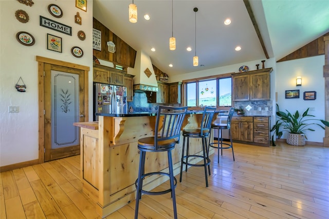 6659 Lamar Trl, Florence, MT 59833 - kitchen with fridge with ice dispenser, custom exhaust hood, a kitchen bar, light wood finished floors, and tasteful backsplash