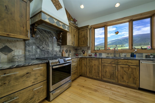 6659 Lamar Trl, Florence, MT 59833 - kitchen featuring stainless steel appliances, custom range hood, dark stone countertops, light wood-style floors, and backsplash