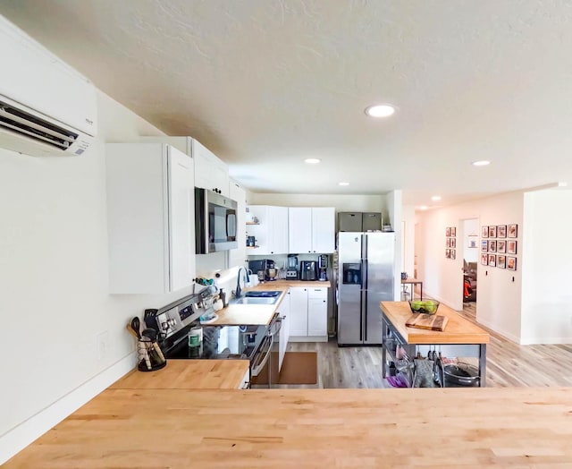 1203 1st St E, Polson, MT 59860 - kitchen with appliances with stainless steel finishes, an AC wall unit, a sink, light wood-type flooring, and white cabinets