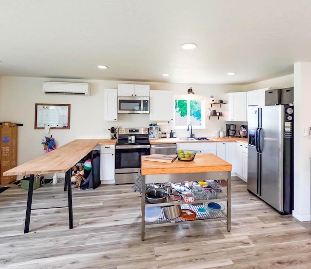 1203 1st St E, Polson, MT 59860 - kitchen with appliances with stainless steel finishes, a sink, a wall mounted AC, light wood-type flooring, and white cabinetry
