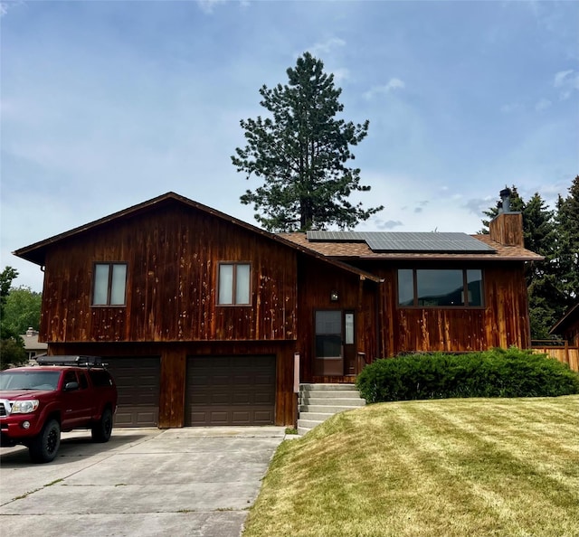 1114 Creek Crossing Rd, Missoula, MT 59802 - view of front of property featuring solar panels, a front yard, concrete driveway, a chimney, and an attached garage